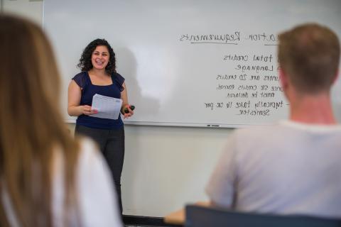 Professor at white board with students looking on in the foreground