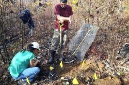 两名研究人员(1名男性站立), 拿着铲子, 1 female squatting next to a whole) work in a prescribed burn site to plant potted red oak trees.